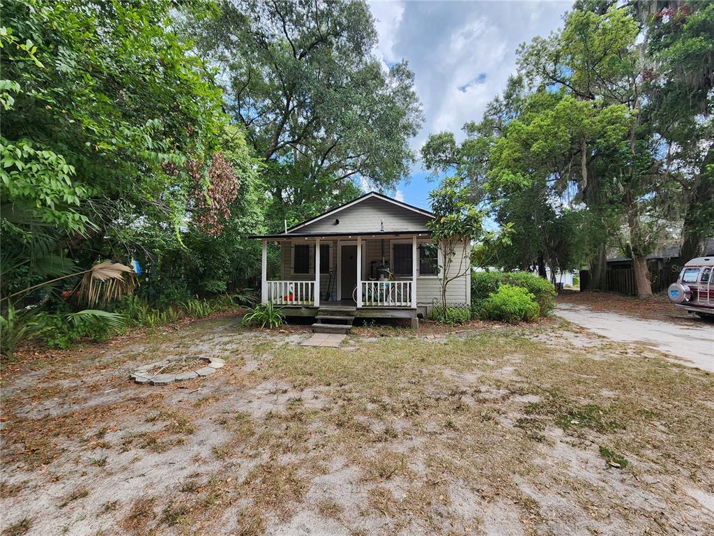 A small, light-colored cottage with a front porch sits on a sandy, wooded lot — 812 SE 4 AVENUE, GAINESVILLE, FL