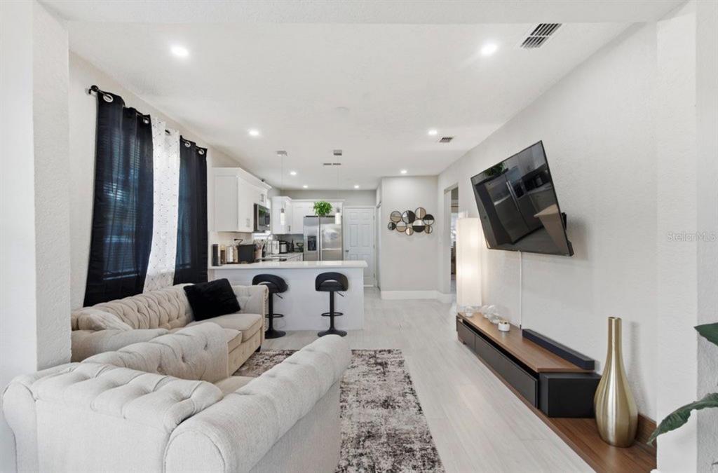 A living room with a tufted sofa, wall-mounted television, and an open kitchen with bar seating — 2717 W CHERRY STREET, TAMPA, FL