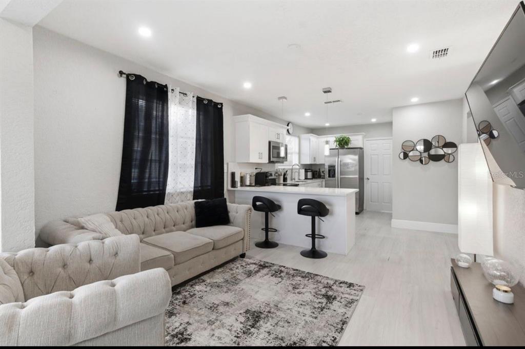 An open-concept living room and kitchen featuring a tufted sofa, breakfast bar, and light flooring — 2717 W CHERRY STREET, TAMPA, FL