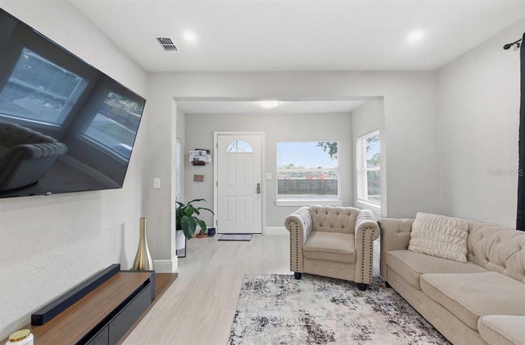 A living room features light wood flooring, a wall-mounted television, and beige tufted furniture — 2717 W CHERRY STREET, TAMPA, FL