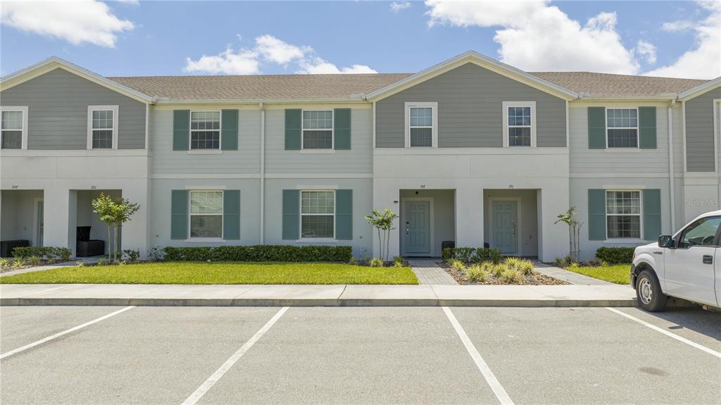 A two-story townhouse exterior features light-colored siding, dark shutters, and a paved parking area — 197 JETTY WAY, DAVENPORT, FL