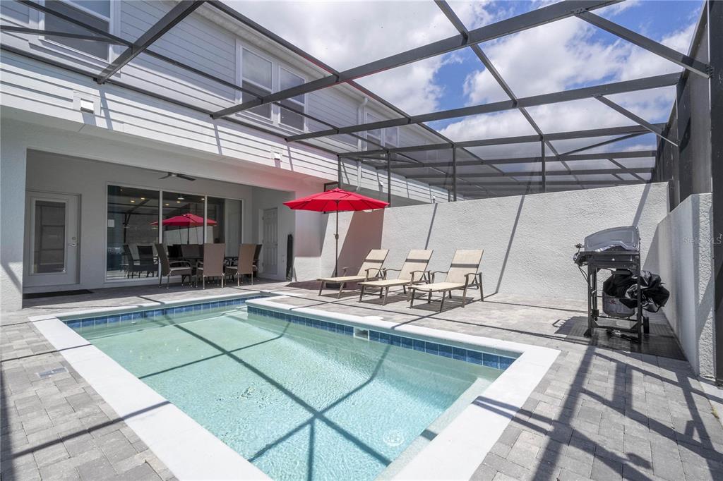 A screened-in patio features a rectangular swimming pool, lounge chairs, a grill, and a red umbrella — 197 JETTY WAY, DAVENPORT, FL