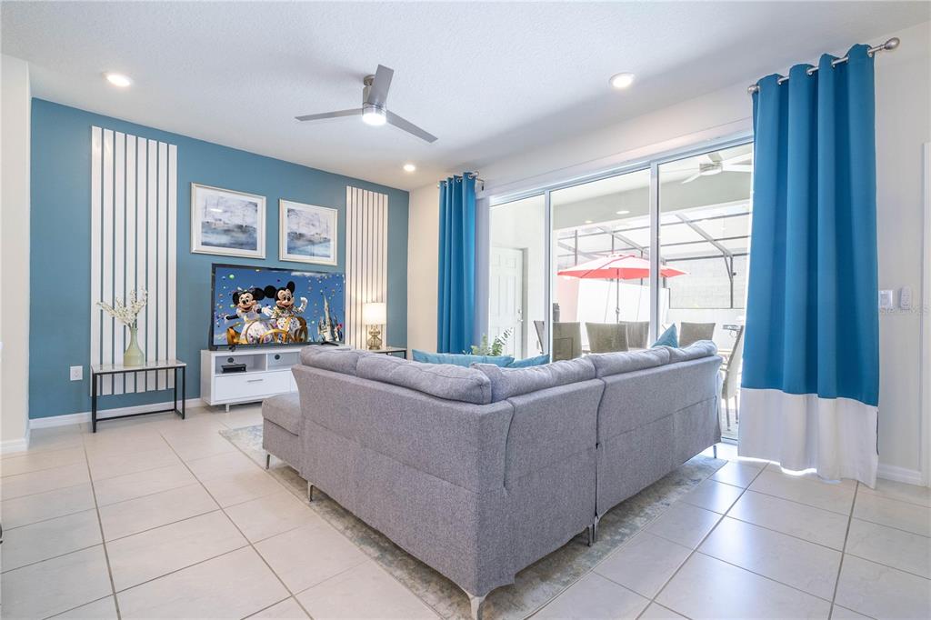 A living room features a gray sectional sofa, blue accent wall, and sliding glass doors — 197 JETTY WAY, DAVENPORT, FL