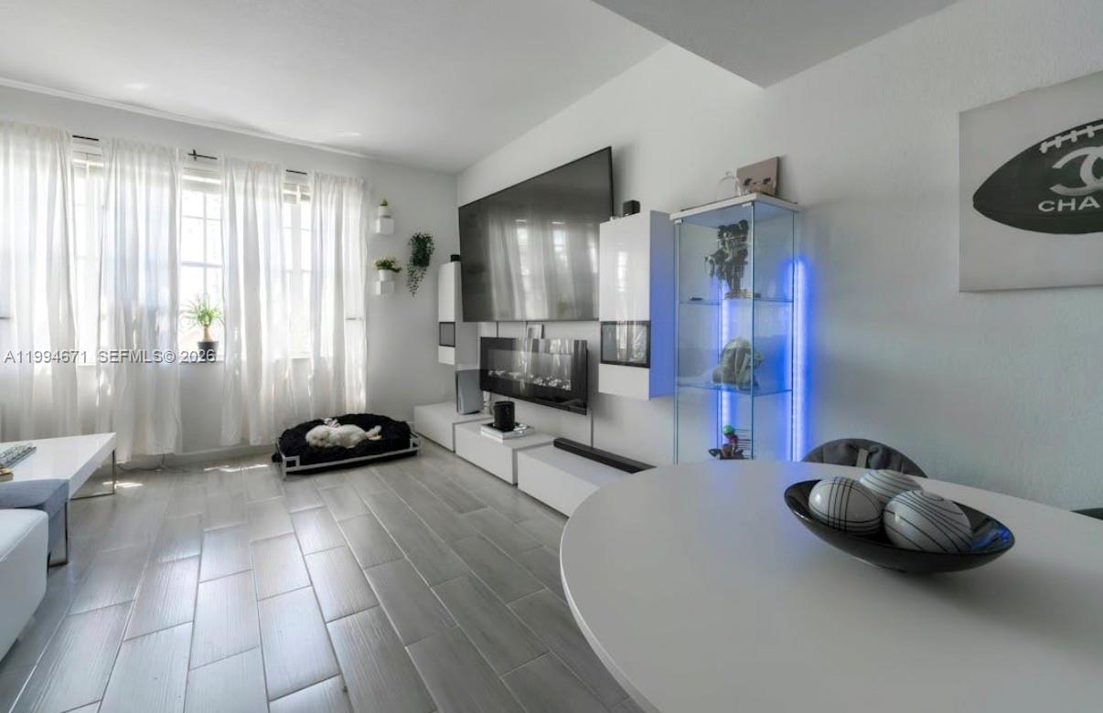 A living room features a wall-mounted television, fireplace, glass display cabinet, and light-colored tile flooring — 705 SW 148th Ave # 202, Sunrise FL 33325, SUNRISE, FL