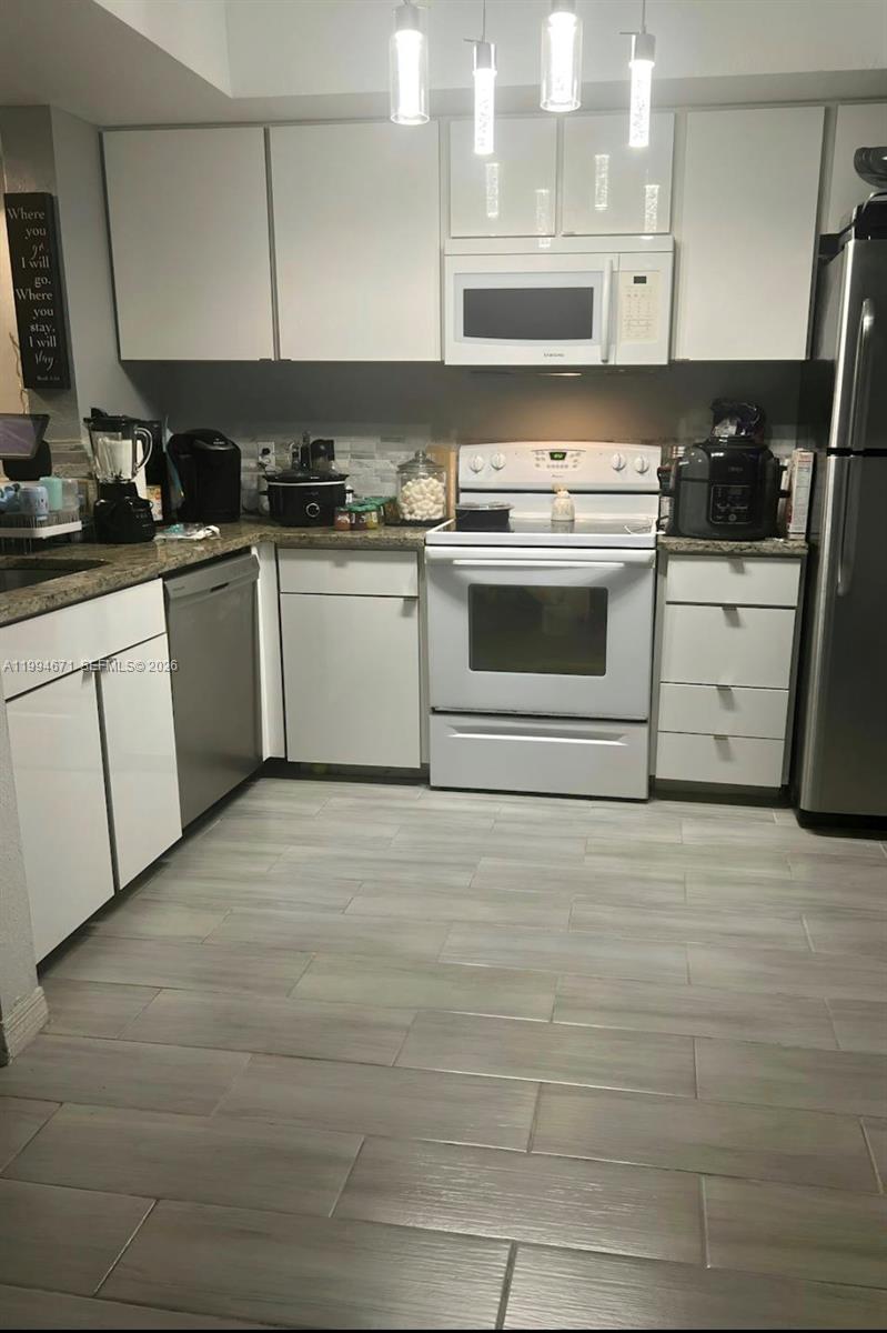 A kitchen features white cabinetry, stainless steel appliances, granite countertops, and light-colored tile flooring — 705 SW 148th Ave # 202, Sunrise FL 33325, SUNRISE, FL