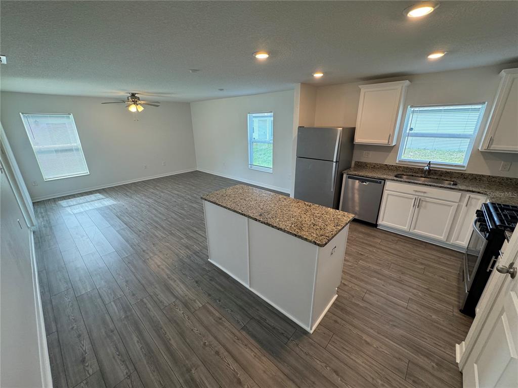 An open-concept kitchen, dining area, and living room featuring wood-look flooring and granite countertops — 233 KENSINGTON VIEW BOULEVARD, WINTER HAVEN, FL