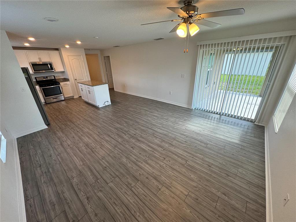 An empty living room features dark wood-look flooring, a ceiling fan, and sliding glass doors — 233 KENSINGTON VIEW BOULEVARD, WINTER HAVEN, FL