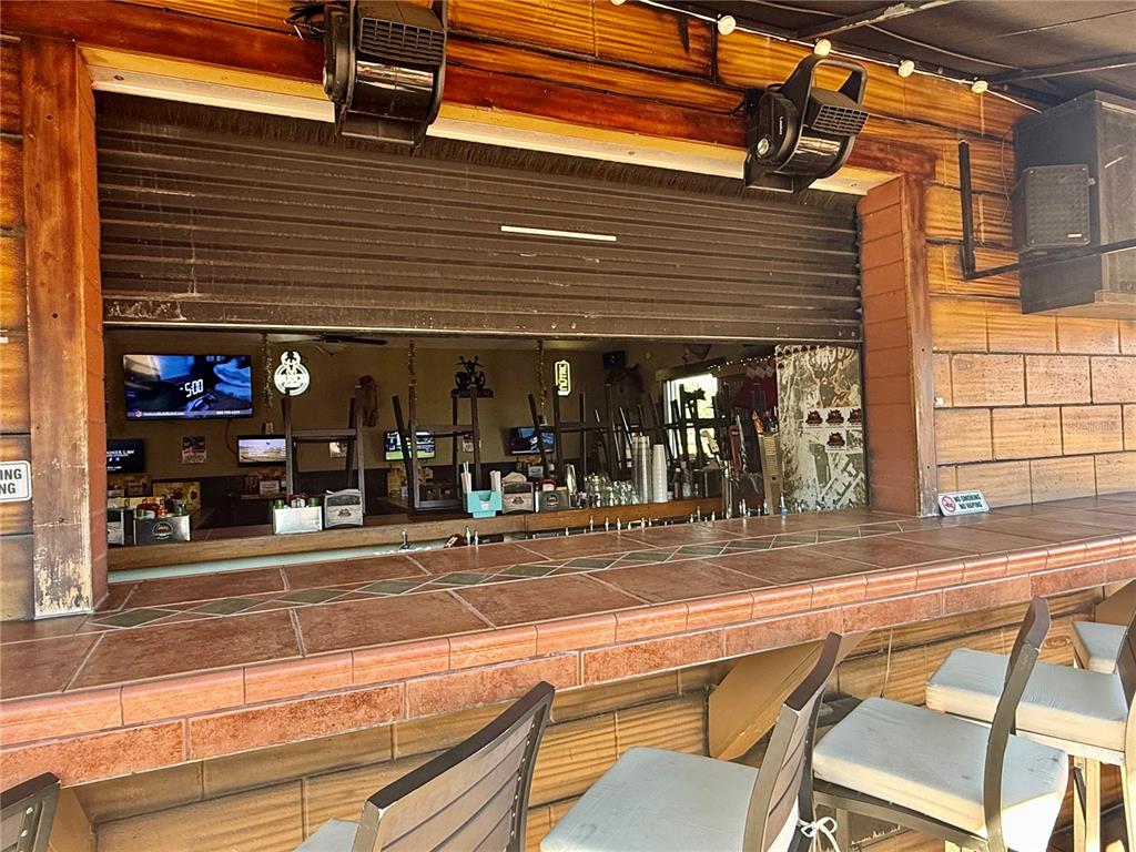 An outdoor bar area features a tiled counter, bar stools, and a roll-down security shutter — 100 S WHITE CEDAR ROAD, SANFORD, FL