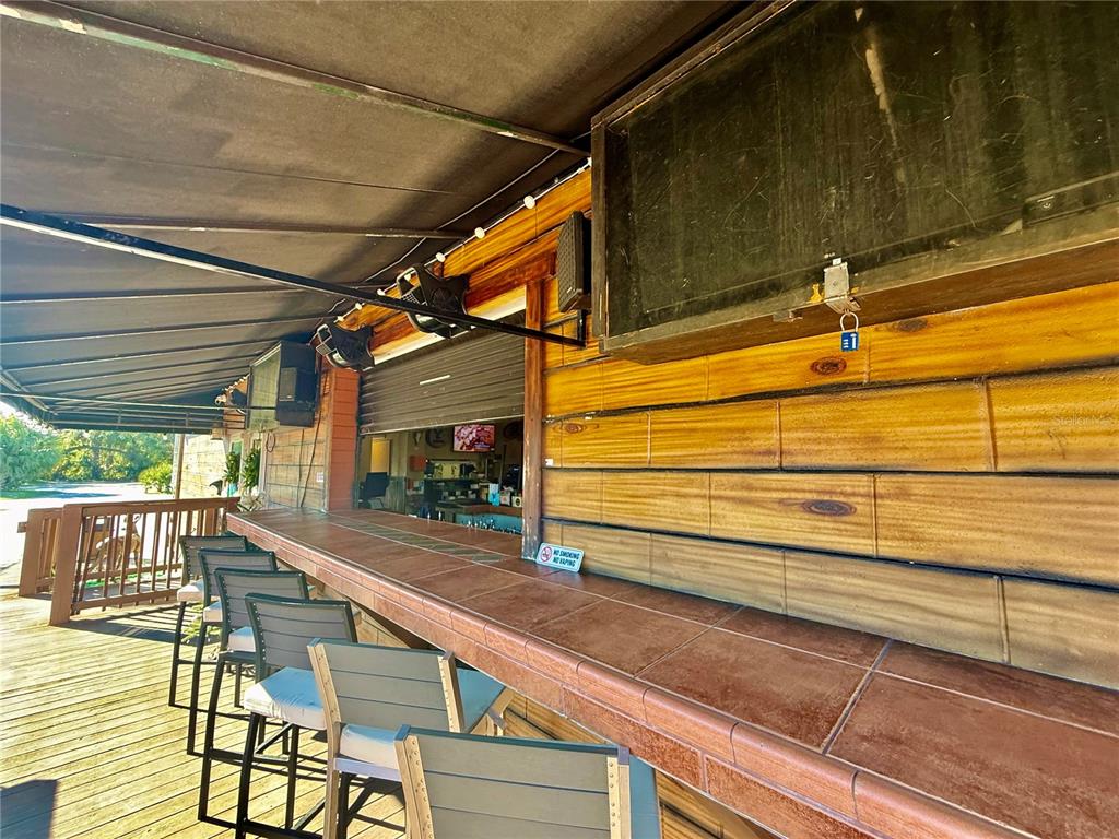 An outdoor bar features a tiled countertop, wooden walls, and several chairs on a deck — 100 S WHITE CEDAR ROAD, SANFORD, FL