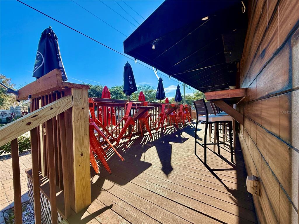 An outdoor wooden deck features red bar stools, tables, and umbrellas under a black awning — 100 S WHITE CEDAR ROAD, SANFORD, FL