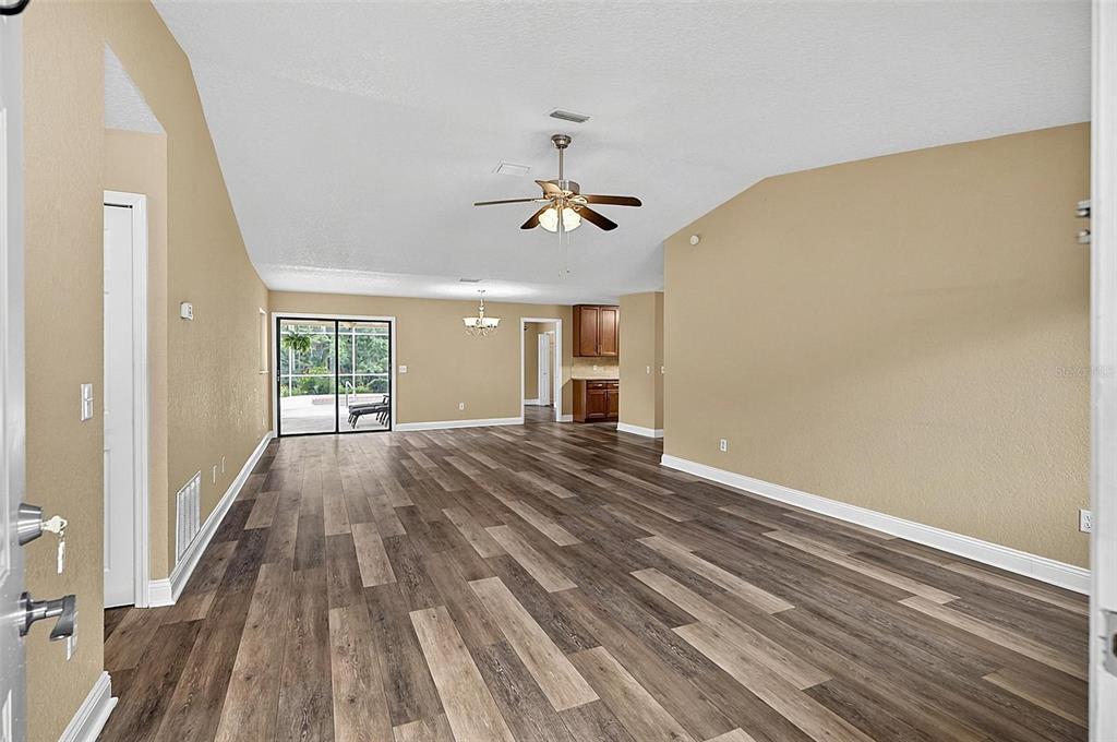 An open-concept living and dining area features vaulted ceilings, wood-look flooring, and a sliding glass door — 43 BAY SPRING PLACE, PALM COAST, FL