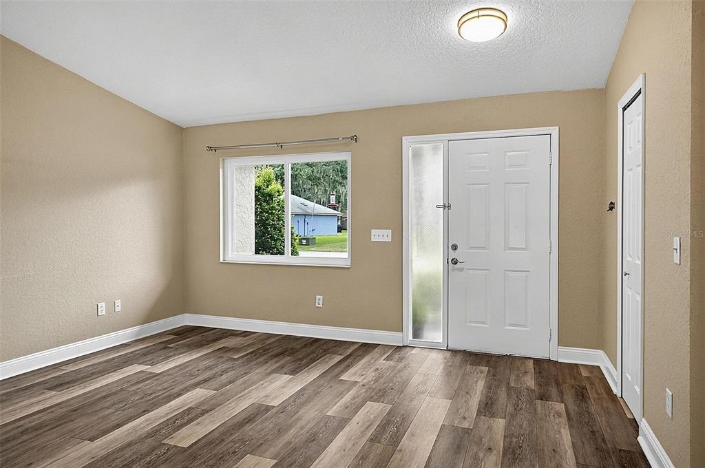 An empty room with tan walls, wood-look flooring, a window, and a white front door — 43 BAY SPRING PLACE, PALM COAST, FL