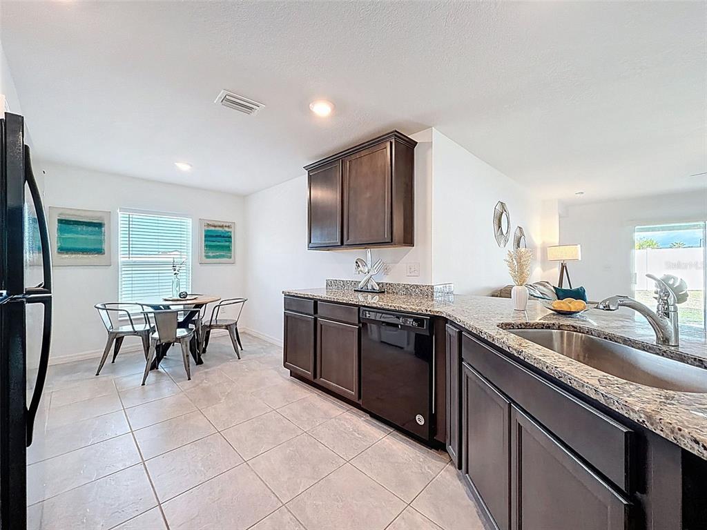 A kitchen with dark wood cabinets, granite countertops, and a dining area with metal chairs — 12943 IMPATIENS STREET, SPRING HILL, FL