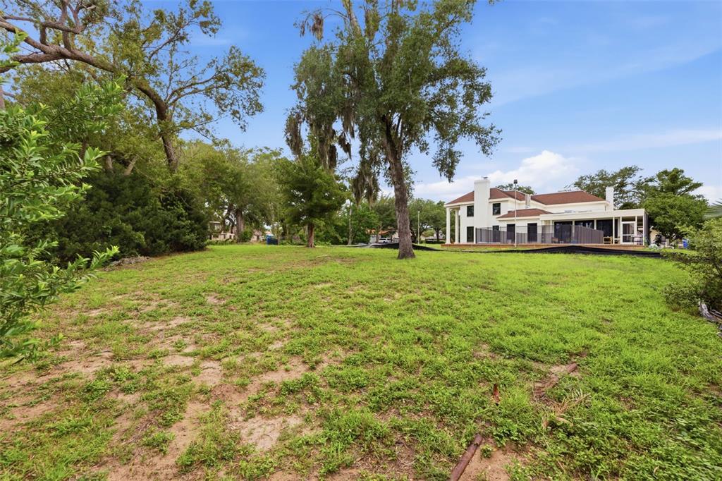 A grassy backyard leads to a two-story house with a screened-in porch and large trees — 40TH AVENUE N, ST PETERSBURG, FL