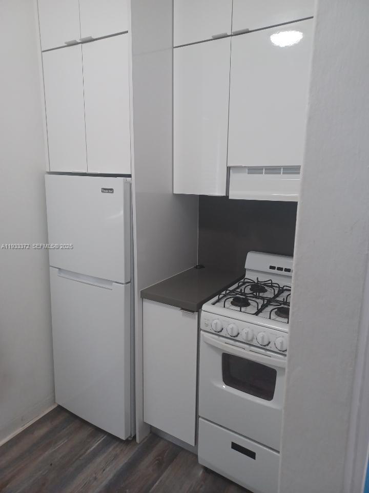A small kitchen features white cabinets, a white refrigerator, and a white gas range — 6950 Byron Ave # 2, Miami Beach FL 33141, MIAMI BEACH, FL
