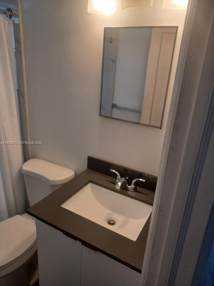 A bathroom features a white vanity with a dark countertop, a mirror, and a toilet — 6950 Byron Ave # 2, Miami Beach FL 33141, MIAMI BEACH, FL
