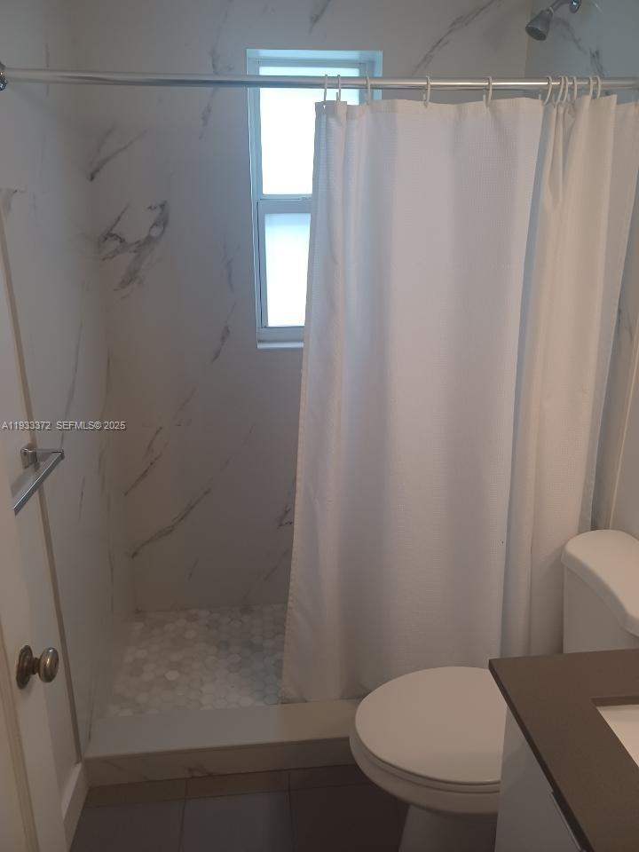 A bathroom features a walk-in shower with marble-look tile and a white shower curtain — 6950 Byron Ave # 2, Miami Beach FL 33141, MIAMI BEACH, FL