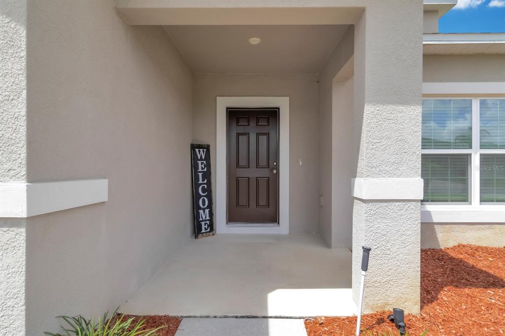 A brown front door with a welcome sign sits under a covered entryway — 4108 DEERMOSS DRIVE, CLERMONT, FL