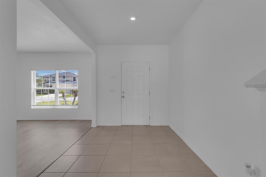 An entryway with light-colored tile flooring leads to a white front door and adjacent living area — 4108 DEERMOSS DRIVE, CLERMONT, FL