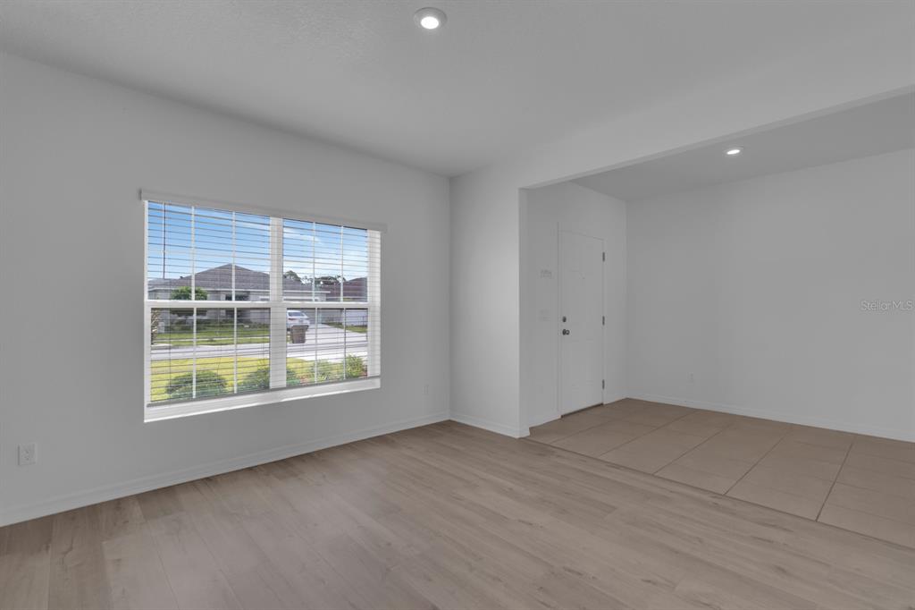 An empty room features light wood-look flooring, a large window, and a tiled entryway — 4108 DEERMOSS DRIVE, CLERMONT, FL