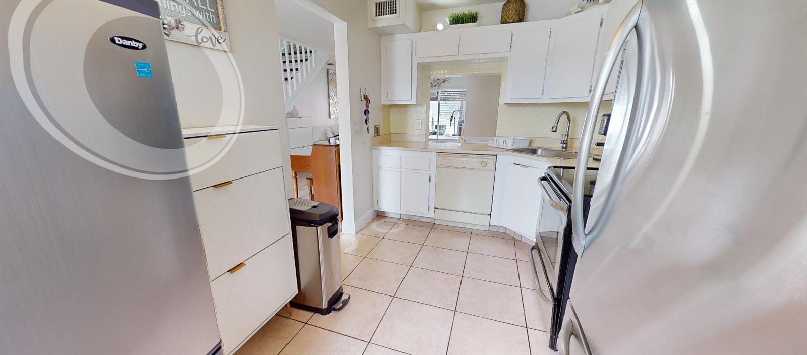 A kitchen features white cabinets, tile flooring, stainless steel appliances, and a pass-through window — 217 Foxtail Drive # G, FL 33415, FL