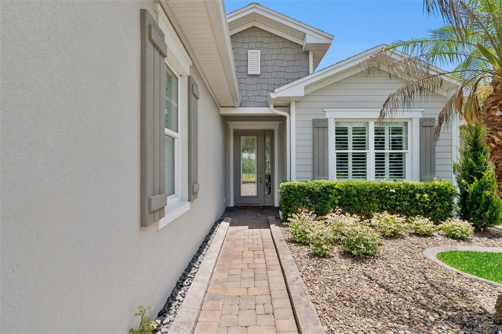 A paved walkway leads to the front entrance of a house with gray siding — 1689 VICTORIA GARDENS DRIVE, DELAND, FL
