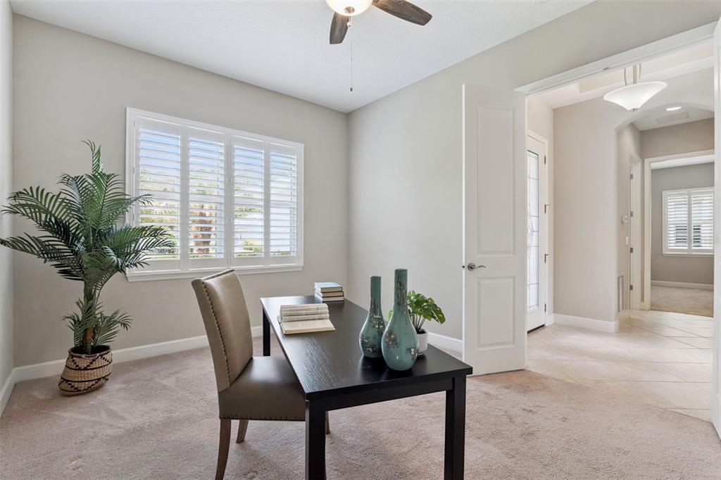 A home office features a dark desk, a chair, a potted plant, and shuttered windows — 1689 VICTORIA GARDENS DRIVE, DELAND, FL
