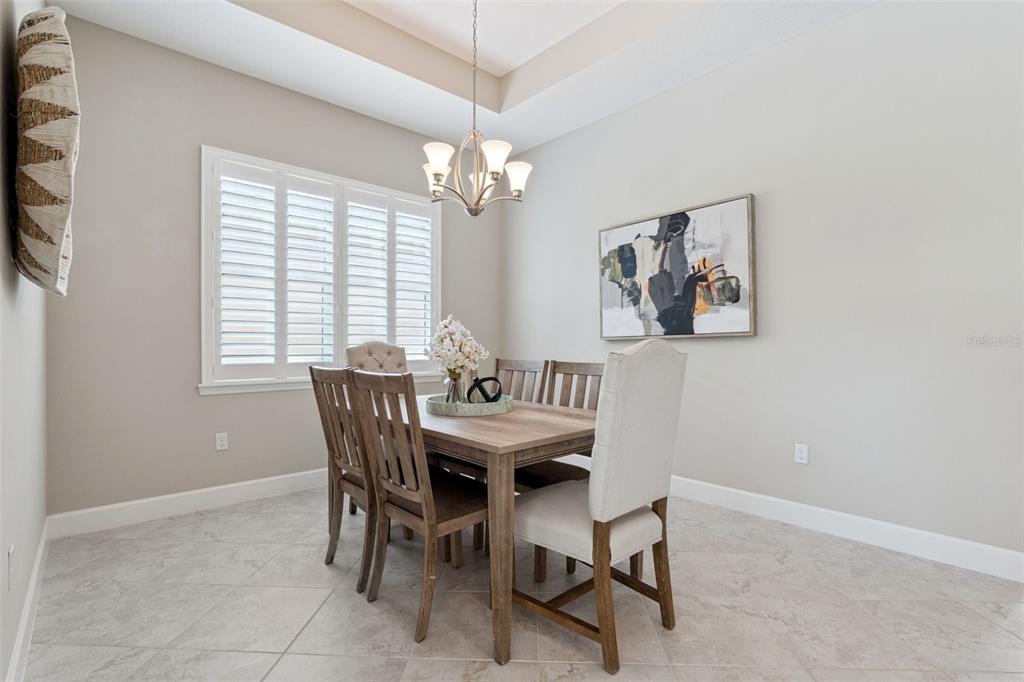 A dining room features a wooden table, upholstered chairs, a chandelier, and plantation shutters — 1689 VICTORIA GARDENS DRIVE, DELAND, FL