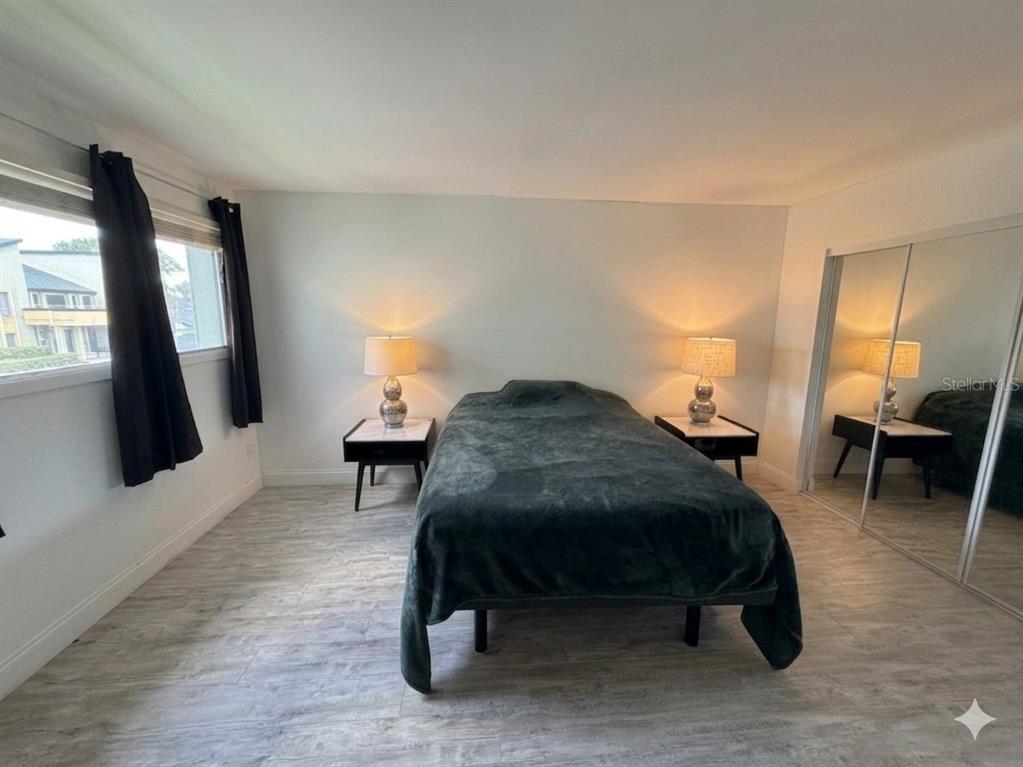 A bedroom features light wood-look flooring, a bed with a dark blanket, and mirrored closets — 924 LAKE DESTINY ROAD UNIT E, ALTAMONTE SPRINGS, FL