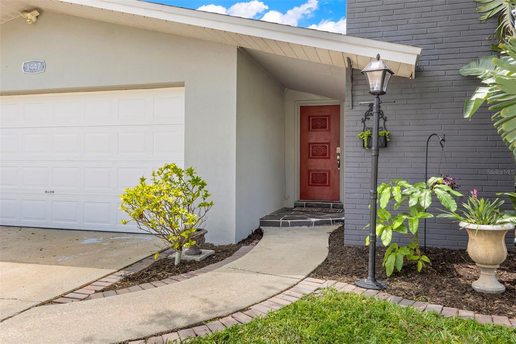 A red front door is recessed next to a white garage and grey brick wall — 1447 BYRAM DRIVE, CLEARWATER, FL