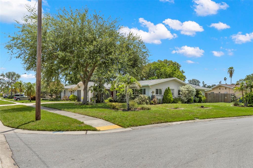 A single-story house with a light-colored exterior sits on a corner lot with trees — 1447 BYRAM DRIVE, CLEARWATER, FL