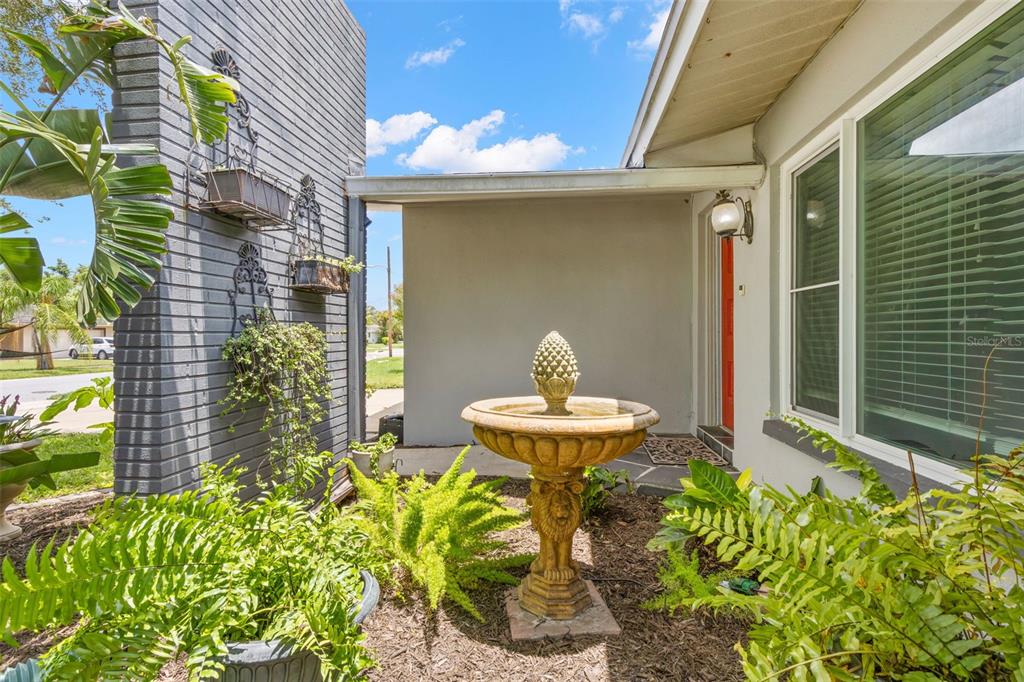 A stone fountain sits in a garden bed in front of a house entrance — 1447 BYRAM DRIVE, CLEARWATER, FL