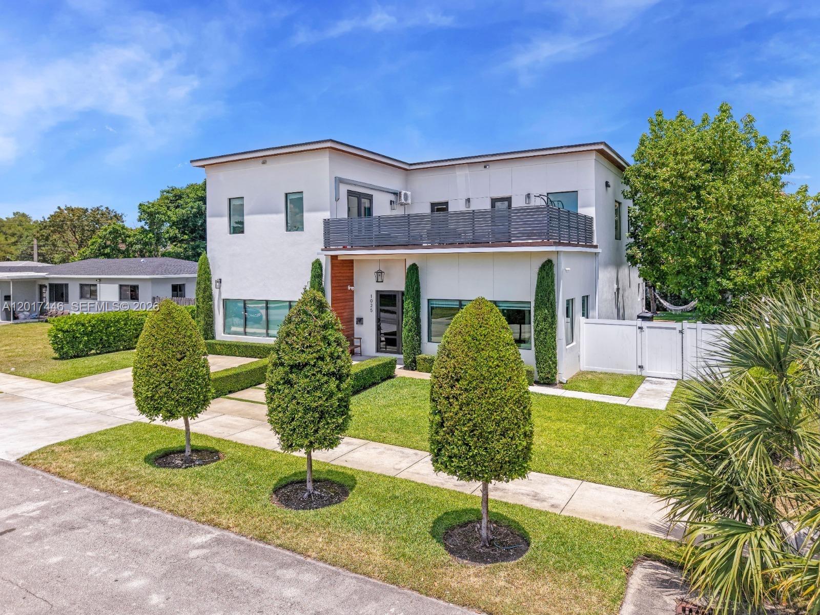 A two-story modern house features a balcony, white stucco exterior, and manicured landscaping — 1025 NE 170th Ter, Miami FL 33162, MIAMI, FL