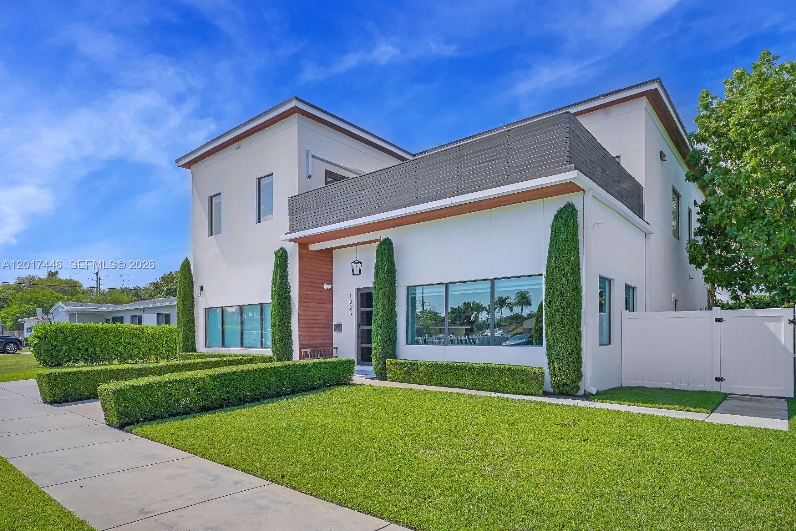 A modern two-story house features white stucco walls, wood accents, and manicured landscaping — 1025 NE 170th Ter, Miami FL 33162, MIAMI, FL