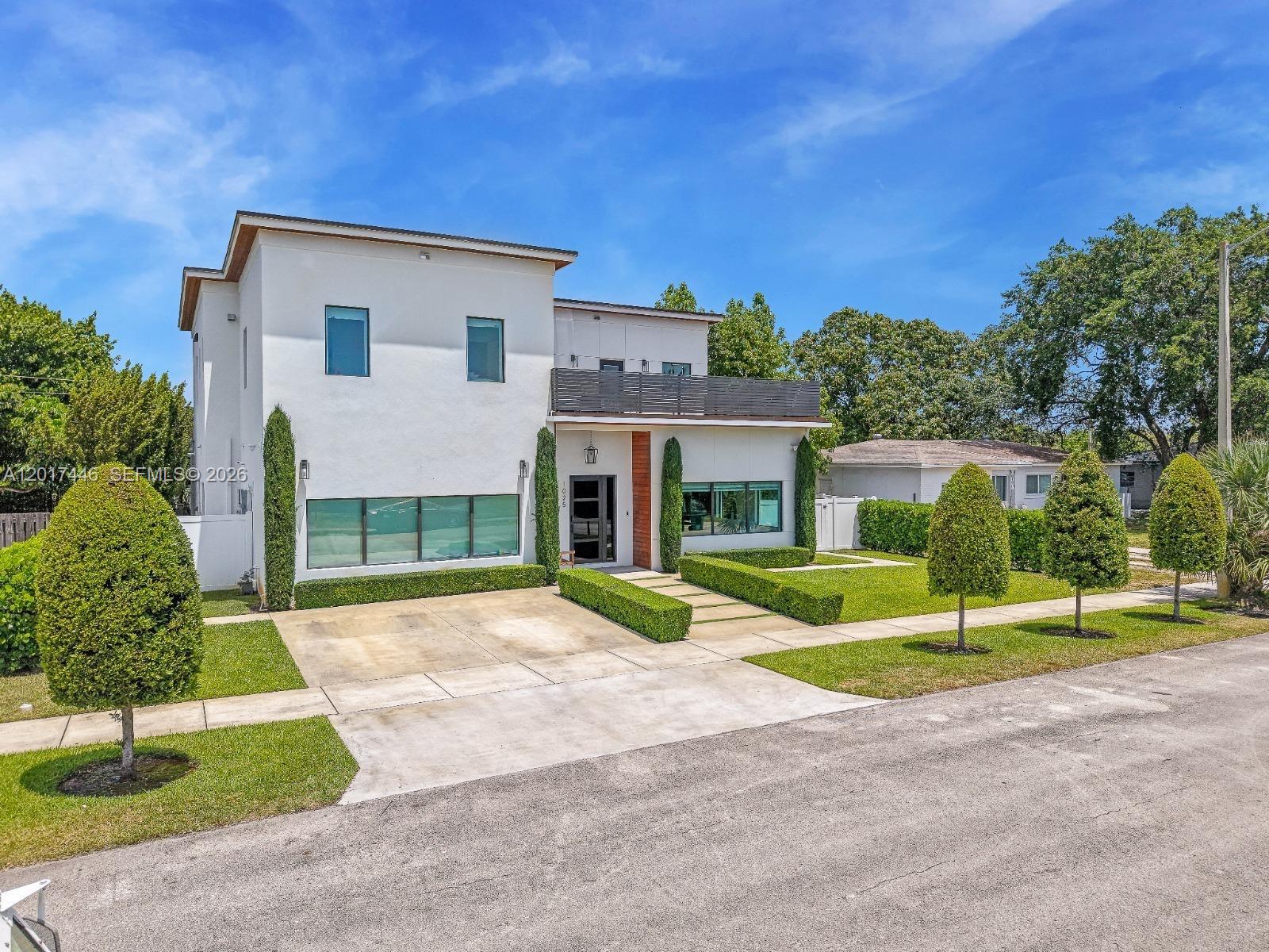 A modern two-story white house features a concrete driveway, manicured hedges, and a balcony — 1025 NE 170th Ter, Miami FL 33162, MIAMI, FL