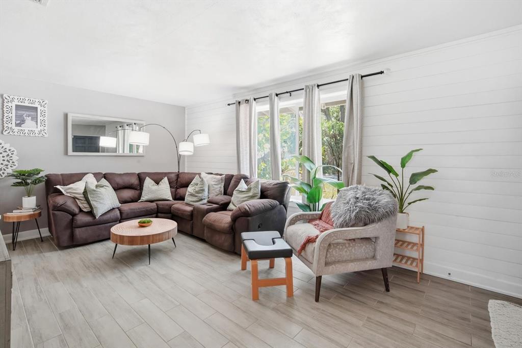 A living room features a brown sectional sofa, an armchair, and white shiplap walls — 3307 3RD AVENUE W, BRADENTON, FL