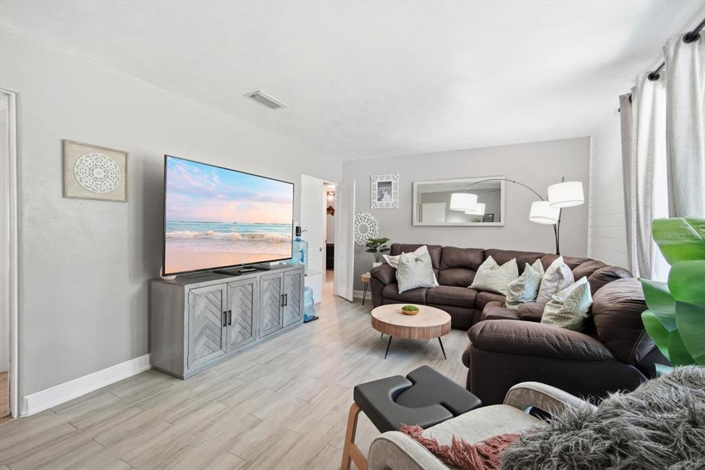 A living room features a sectional sofa, a television on a console, and light flooring — 3307 3RD AVENUE W, BRADENTON, FL