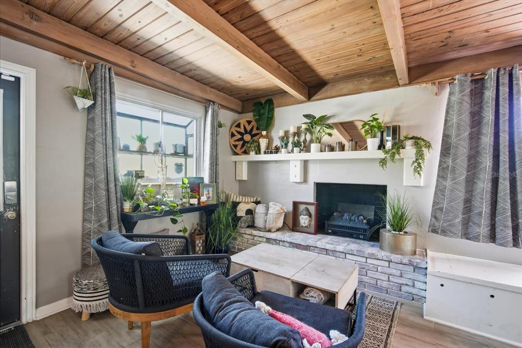 A living room features a brick fireplace, wood-beamed ceiling, and two dark woven armchairs — 3307 3RD AVENUE W, BRADENTON, FL