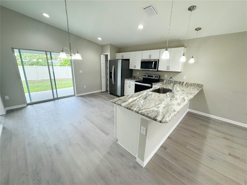 A kitchen features white cabinets, granite countertops, stainless steel appliances, and light wood-look flooring — 6574 SE 108TH STREET, BELLEVIEW, FL