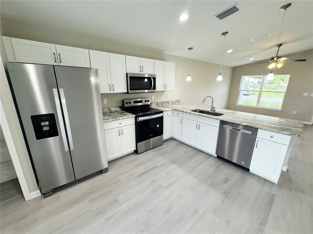 A modern kitchen features white cabinets, stainless steel appliances, and light wood-look flooring — 6574 SE 108TH STREET, BELLEVIEW, FL