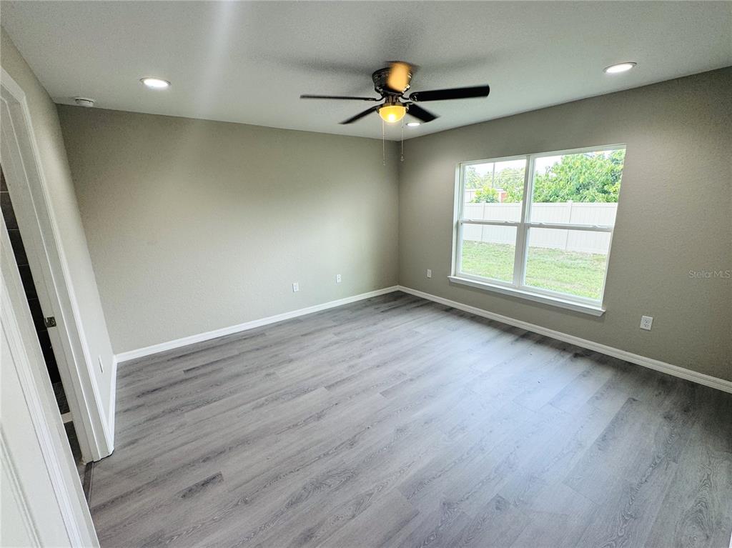 An empty bedroom features gray wood-look flooring, a ceiling fan, and a large window — 6574 SE 108TH STREET, BELLEVIEW, FL