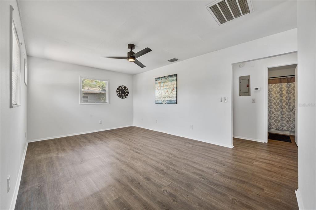An empty room with wood-look flooring, white walls, a ceiling fan, and a bathroom doorway — 3419 N 54TH STREET, TAMPA, FL