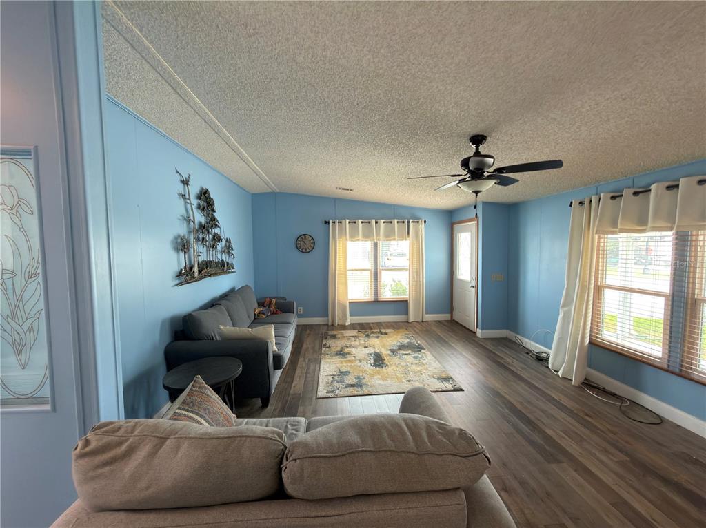 A living room with blue walls, wood-look flooring, a ceiling fan, and two gray sofas — 141 VICTORIA DRIVE, HAINES CITY, FL