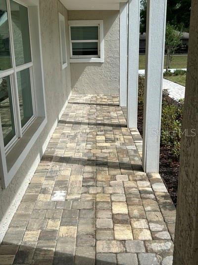 A covered patio features paver flooring, white columns, and a window on the exterior wall — 8422 NW 2ND STREET, OCALA, FL