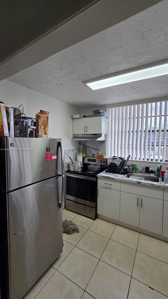 A kitchen features stainless steel appliances, white cabinets, a tiled floor, and a window with blinds — 1748 NW 55th Ave # 101, Lauderhill FL 33313, LAUDERHILL, FL