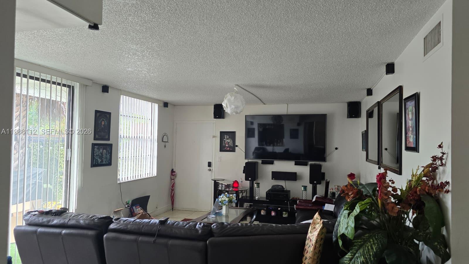 A living room features a large wall-mounted television, surround sound speakers, and a leather sofa — 1748 NW 55th Ave # 101, Lauderhill FL 33313, LAUDERHILL, FL