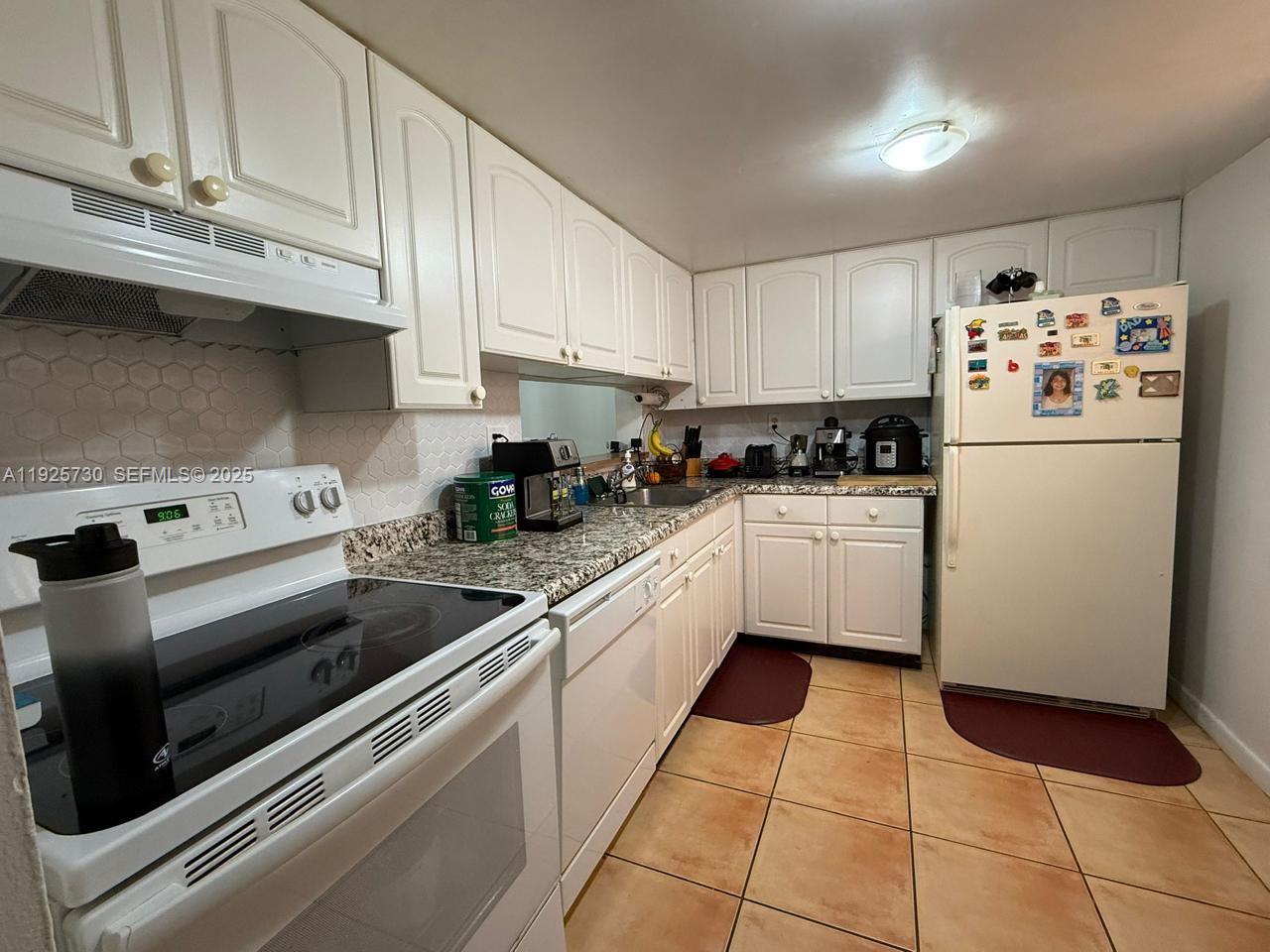 A kitchen features white cabinets, granite countertops, a white stove, and tiled flooring — 8600 SW 133rd Ave Rd # 310, Miami FL 33183, MIAMI, FL