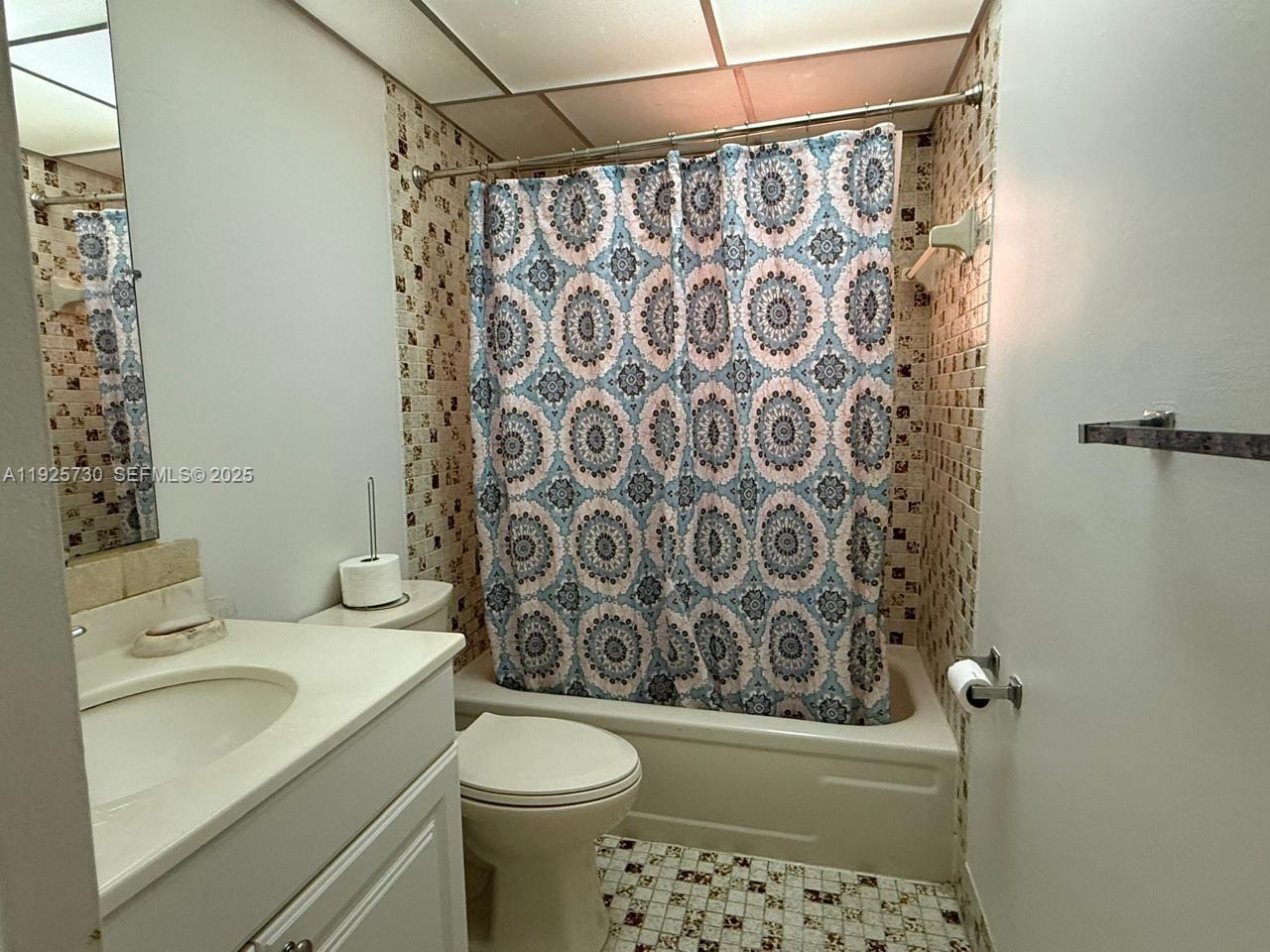 A bathroom features a patterned shower curtain, a white vanity, and tiled walls and floors — 8600 SW 133rd Ave Rd # 310, Miami FL 33183, MIAMI, FL