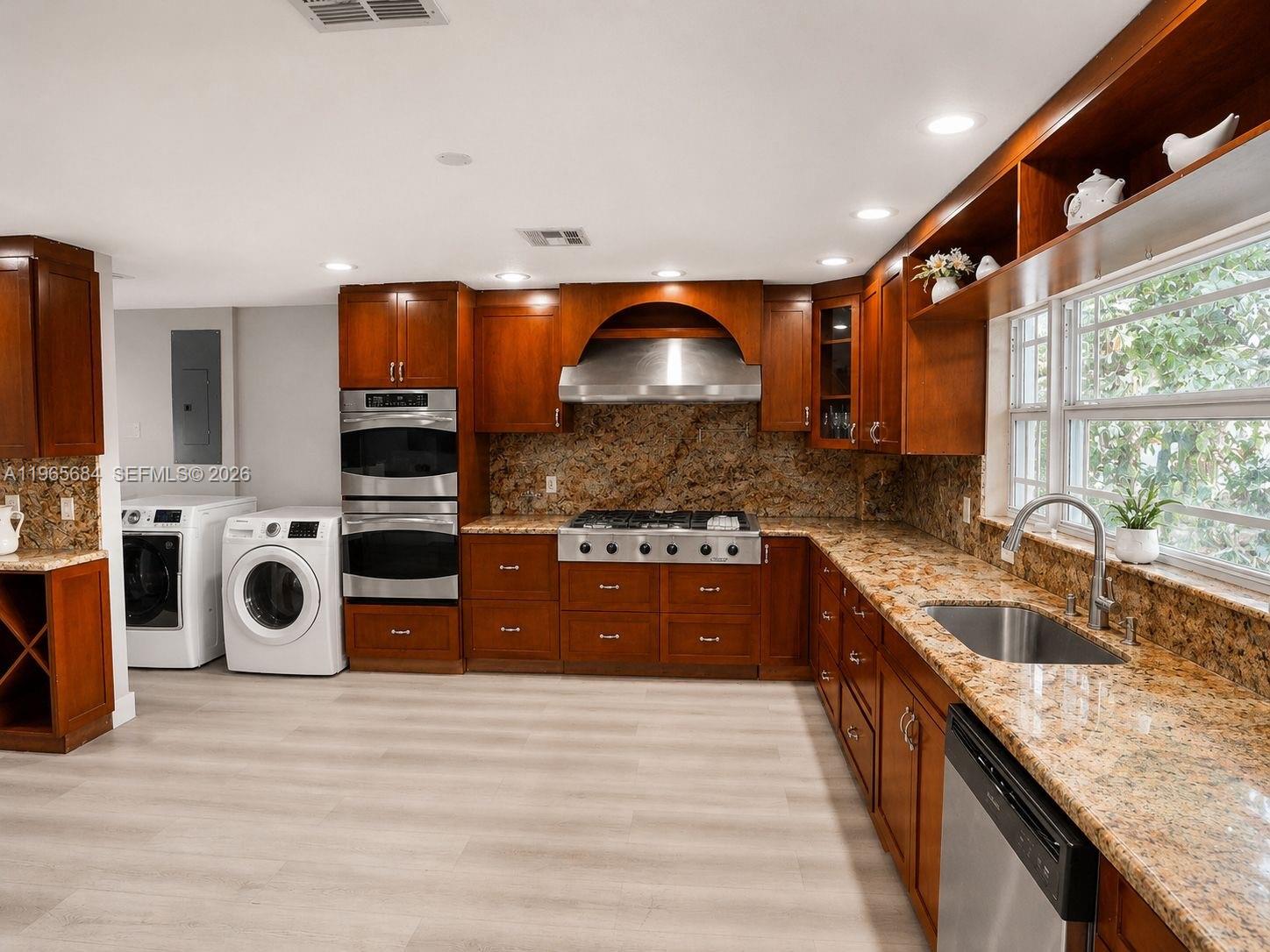 A kitchen features wood cabinetry, granite countertops, stainless steel appliances, and a laundry area — 901 SW 121 AVE, Davie FL 33325, DAVIE, FL