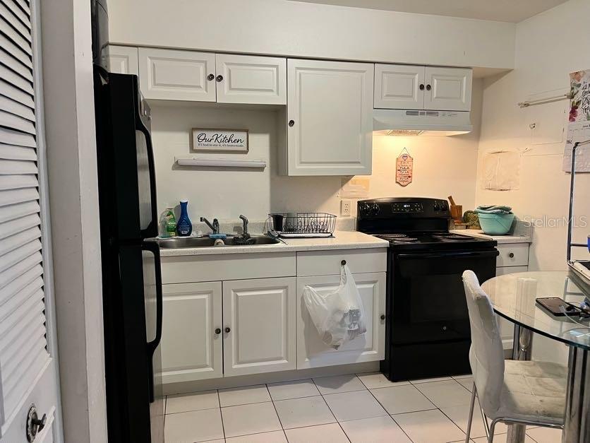 A kitchen with white cabinets, a black refrigerator, a black stove, and a glass dining table — 5885 DAHLIA DRIVE UNIT 24, ORLANDO, FL